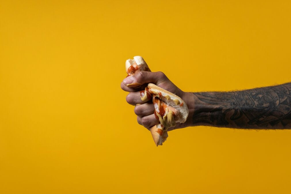 A black person's arm squeezing and destroying a UPF fast food hot dog.