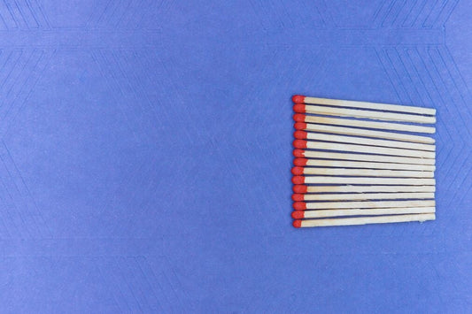 A bright blue background with a vertical stack of unlit matches with red tips