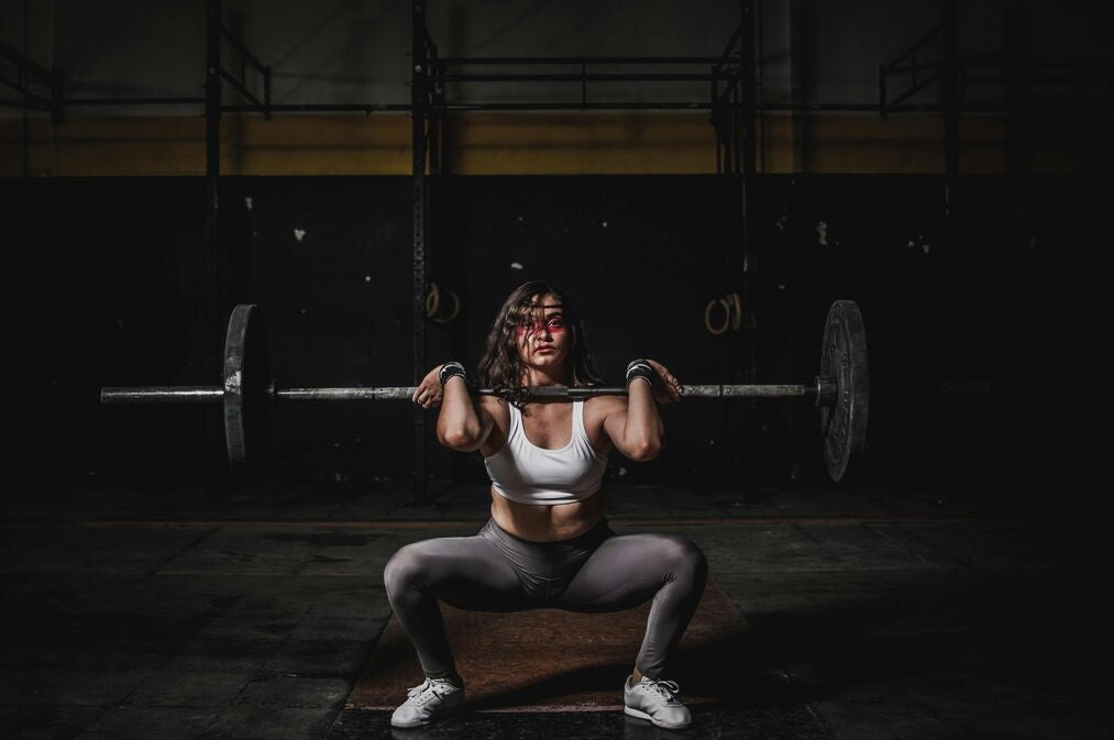 A professional body builder, female, performing a barbell press in a moodily-lit gym.