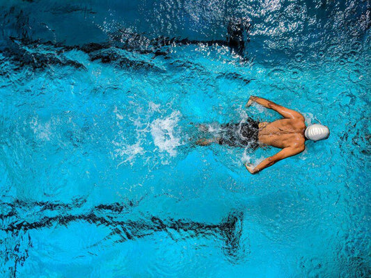 A professional swimmer in a bright blue pool, photographed from above as they swim in a butterfly style.